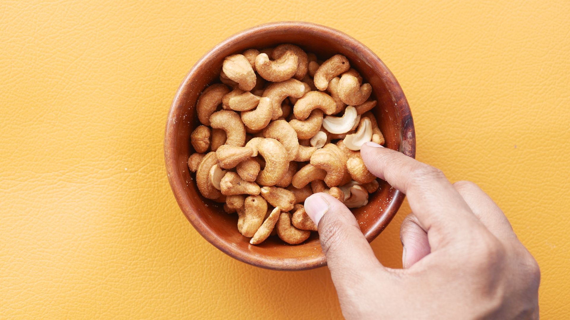 Vrouwenhand die cashews uit een schaaltje pakt