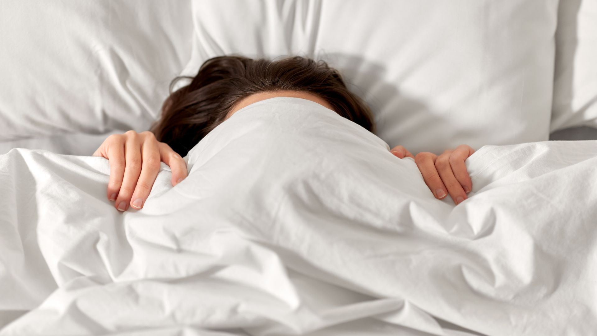 Vrouw die zich verstopt onder het dekbed - symbool voor geen duidelijke keuzes maken